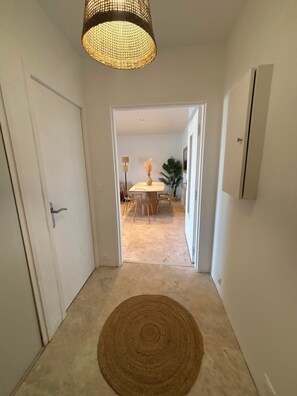 A hallway with a round rug, a door on the left, and a dining area in the background. - Spacious, luxury 3-bedroom apartment with ocean views and a pool (Bormes-les-Mimosas)