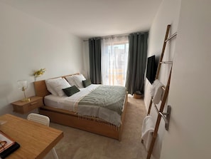 A hotel room with a bed, bedside table, chair, TV, and a view of the outdoors. - Spacious, luxury 3-bedroom apartment with ocean views and a pool (Bormes-les-Mimosas)