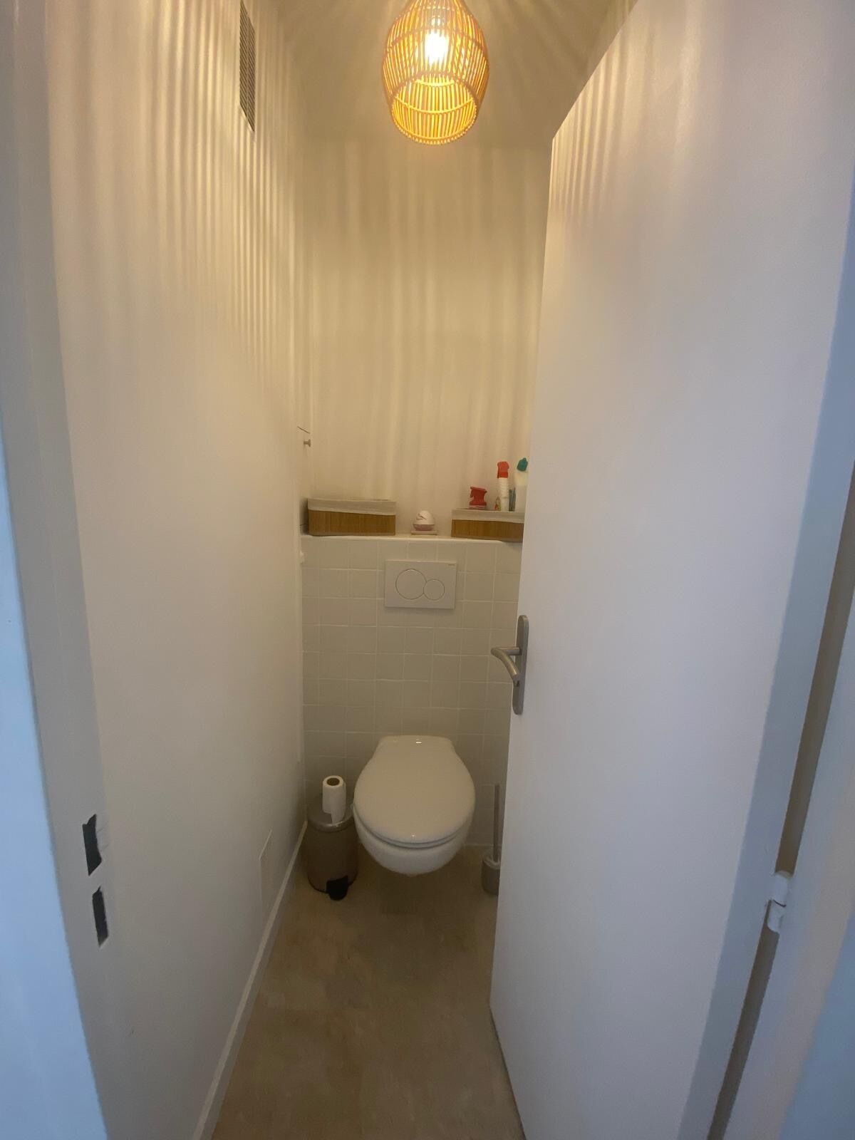 A small, narrow bathroom with a toilet, a toilet paper holder, and a trash bin.