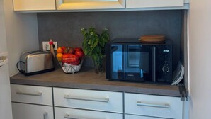 Una cocina con armarios blancos, un tostador, un bol de fruta, una planta en maceta y un microondas negro.
