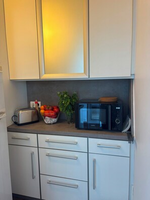 Eine Küche mit weißen Schränken, einem Toaster, einer Obstschale, einer Topfpflanze und einer schwarzen Mikrowelle.