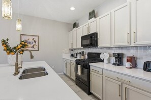A modern kitchen with white cabinets, stainless steel appliances, and a white countertop. - 4735 Solterra Resort 4BR Pool House near Disney (Davenport)