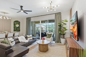 A modern living room with a sofa, coffee table, and a TV. There is a balcony with a view. - 4735 Solterra Resort 4BR Pool House near Disney (Davenport)