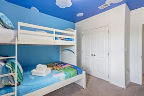 Ein Stockbett mit farbenfroher Bettdecke, ein weißer Kleiderschrank und eine Tür mit Griff.