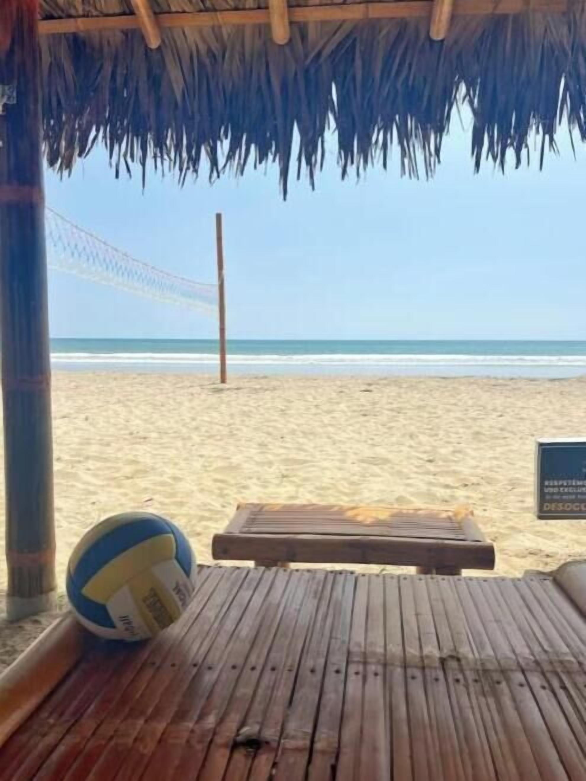 Strandudsigt med en volleyball, en træbænk og et skilt.