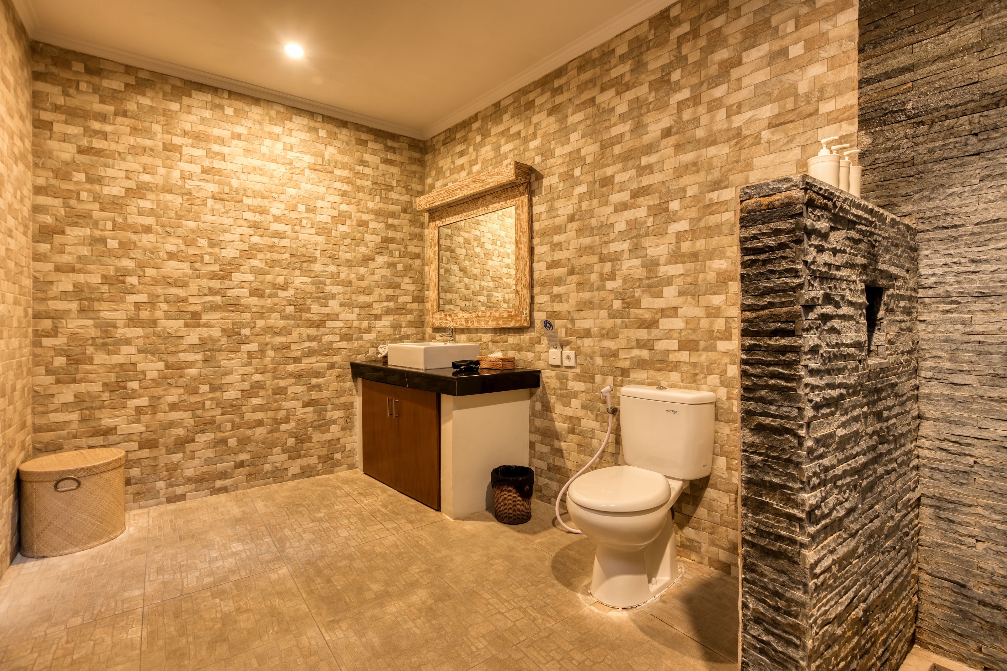 A bathroom with a stone-patterned wall, a wooden cabinet, a toilet, and a sink.