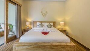 A hotel room with a large bed, two bedside tables with lamps, a dreamcatcher on the wall, and a view of the outside. - Villa Dion Bali (Badung)