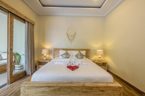 Ein Hotelzimmer mit einem großen Bett, zwei Nachttischen mit Lampen, einem Traumfänger an der Wand und Blick ins Freie.