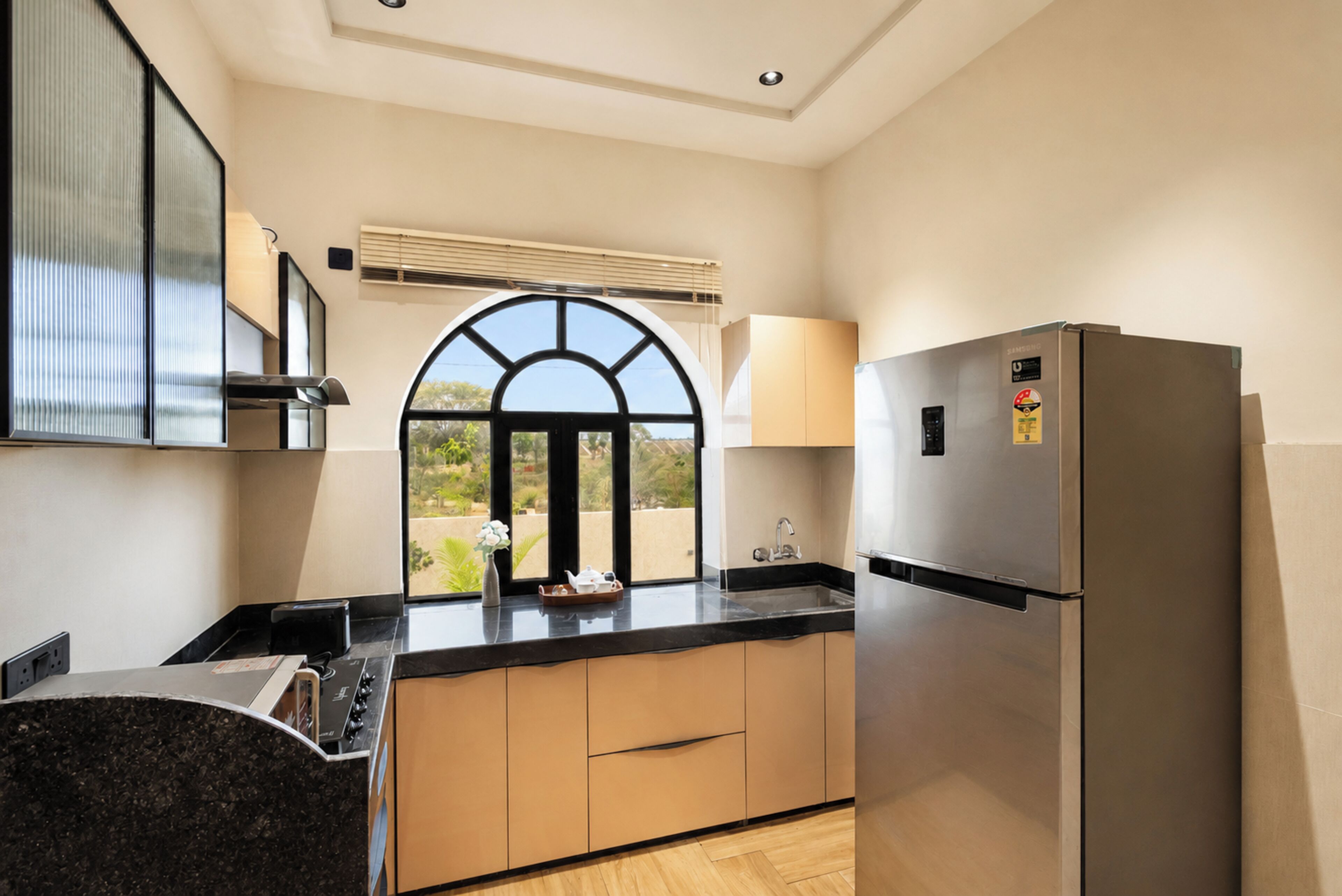 A modern kitchen with a stainless steel refrigerator, a window with a view, and a countertop with a kettle and teapot.