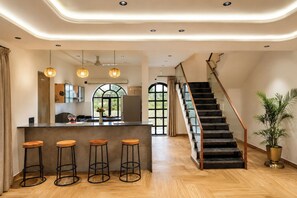 Une cuisine moderne dotée d’un îlot central, de tabourets de bar et d’un escalier avec une rampe en verre.