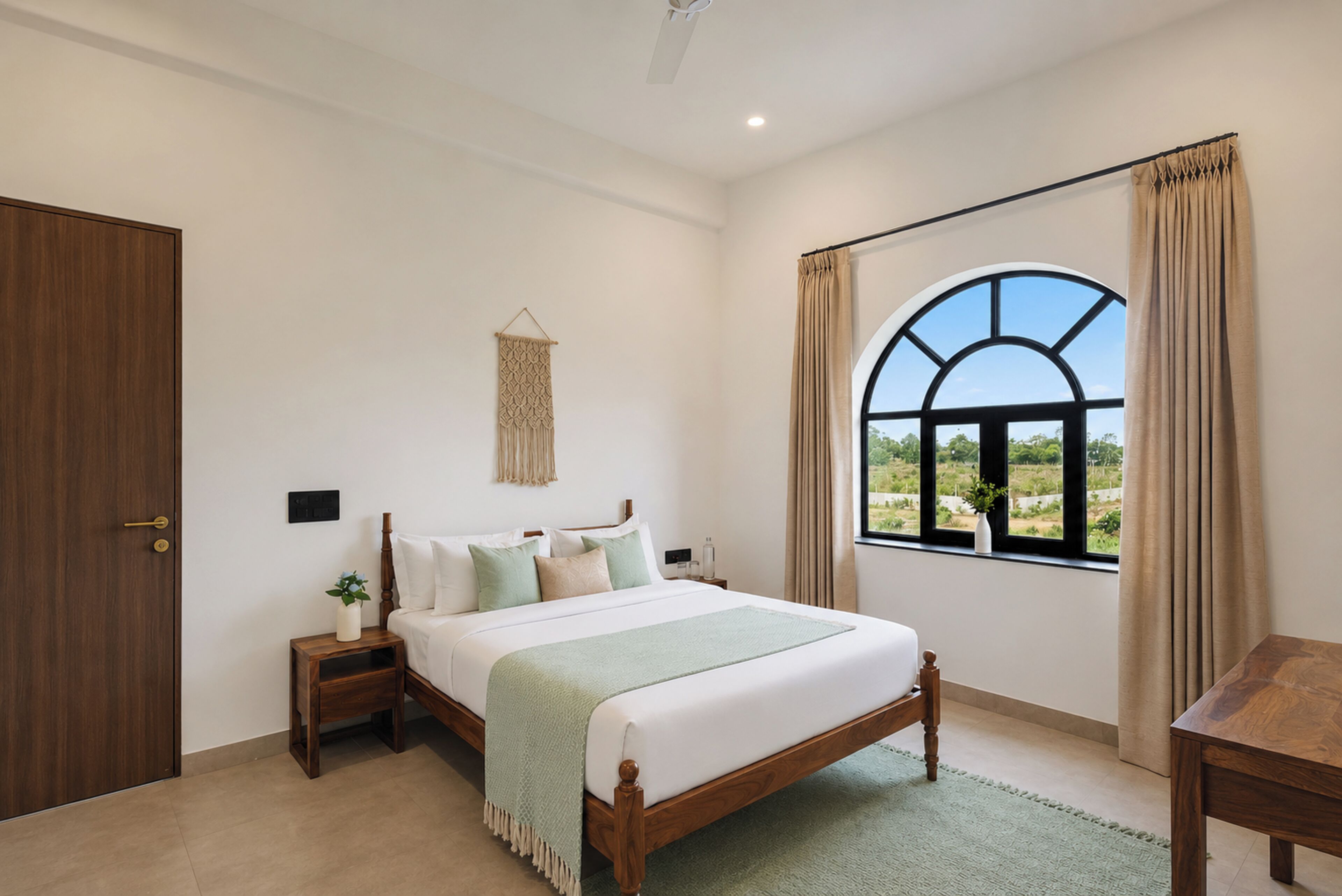 A bedroom with a bed, bedside tables, a wall-mounted macrame piece, a window with curtains, and a view of greenery outside.