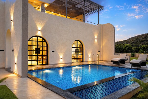 A modern building with a swimming pool, outdoor seating, and a view of the surrounding landscape.
