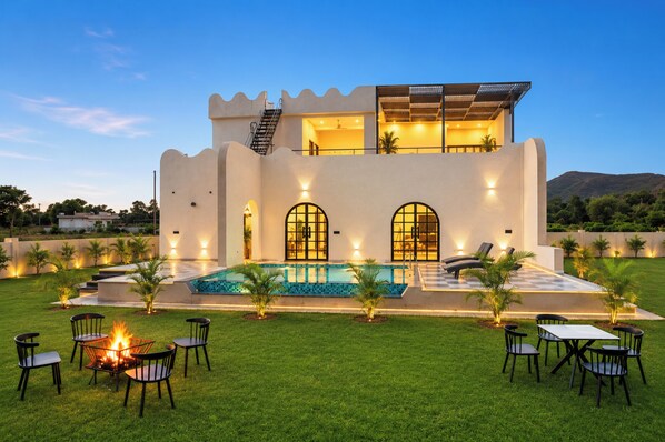 A modern two-story house with a swimming pool, outdoor seating, and a fire pit.
