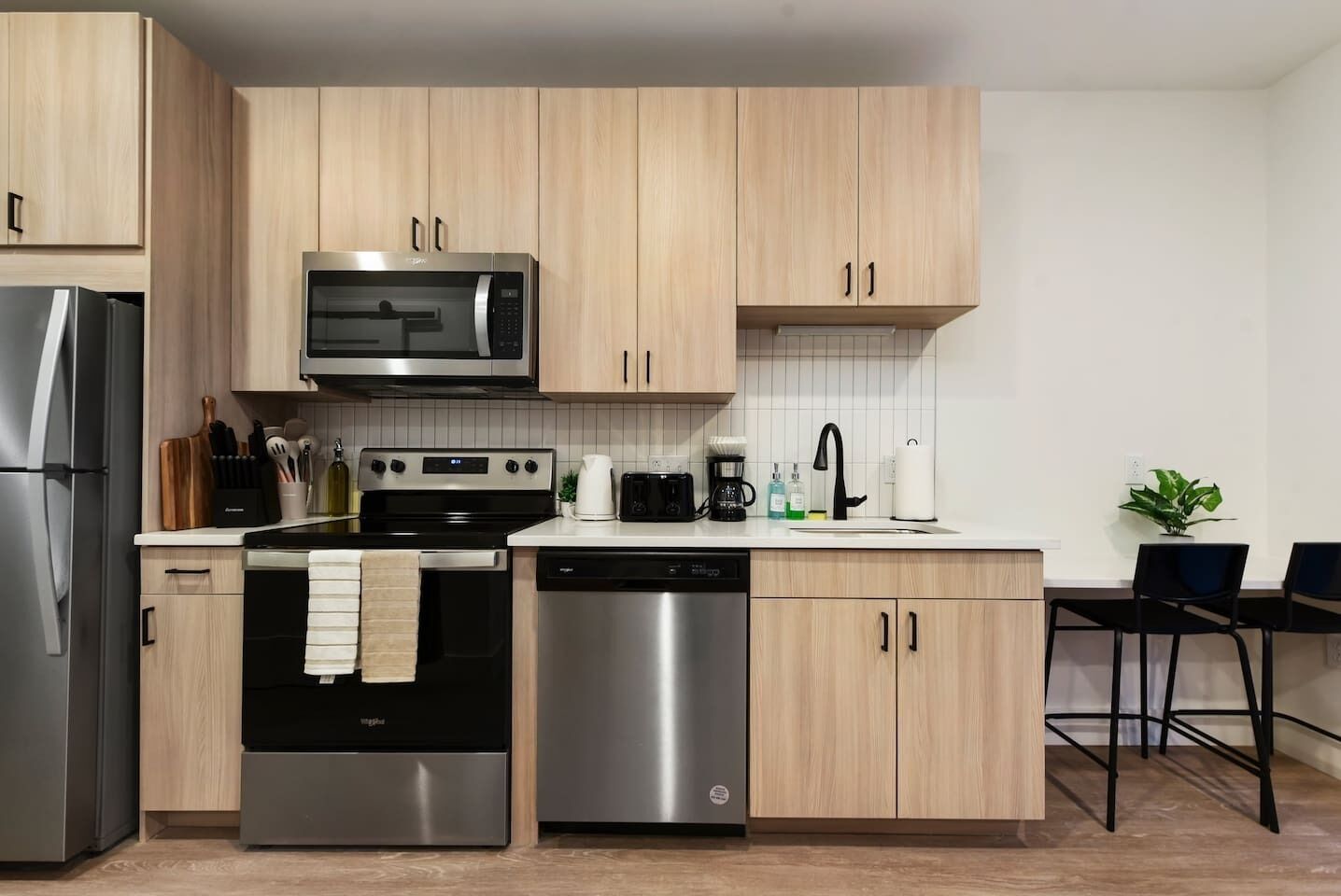 A modern kitchen with stainless steel appliances, wooden cabinets, and a dining area with two chairs.