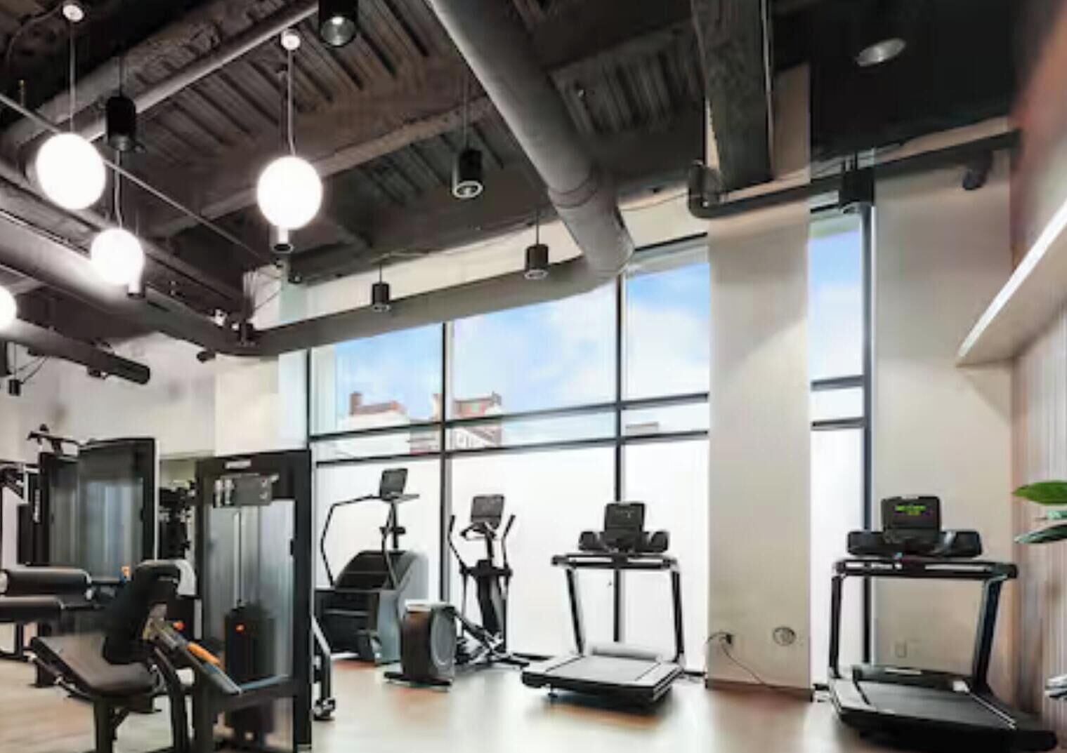 A gym with exercise equipment, large windows, and a high ceiling.