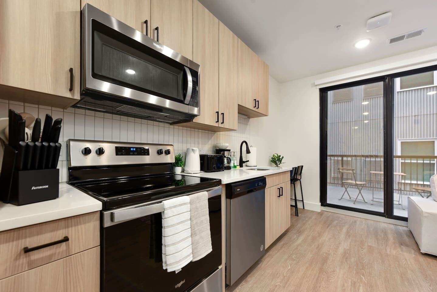 Eine moderne Küche mit Edelstahlgeräten, Holzschränken und einer großen Schiebeglasdoor zum Balkon.
