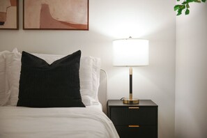 A neatly made bed with a black pillow, a bedside lamp, and a small nightstand with drawers. - Modern Apt w/ HULU, Gym & Parking Near Restaurants (Pittsburgh)