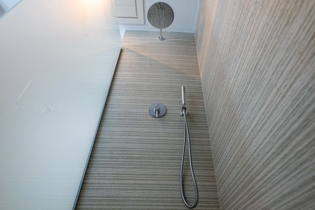 Zona de ducha con cabezal de ducha de mano y panel de control en la pared.