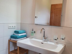 Ein Badezimmer mit einem weißen Waschbecken, einem Holzboden mit gefalteten Handtüchern, einem Spiegel und einer Holztür.