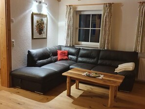 Ein Wohnzimmer mit einem schwarzen Ledersofa, einem Holztisch, einem gerahmten Bild an der Wand und einem Fenster mit Vorhängen.