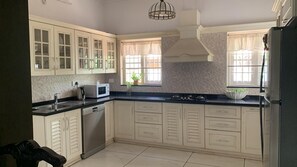 A kitchen with white cabinets, a microwave, a dishwasher, and a stove. - Family Friendly Private Pool Villa, Kochi Near Kadamakudi and Lulu (Varapuzha)