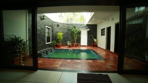 A modern indoor swimming pool with a tiled floor, surrounded by potted plants and a glass wall. - Family Friendly Private Pool Villa - Home Stay, Kochi Near Kadamakudi and Lulu (Varapuzha)