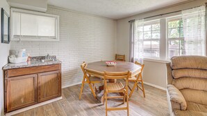A dining area with a wooden table and chairs, a kitchen with a white brick backsplash, and a window with curtains. - 1 Mi to Table Rock Lake! Home w/ Water Views (Shell Knob)