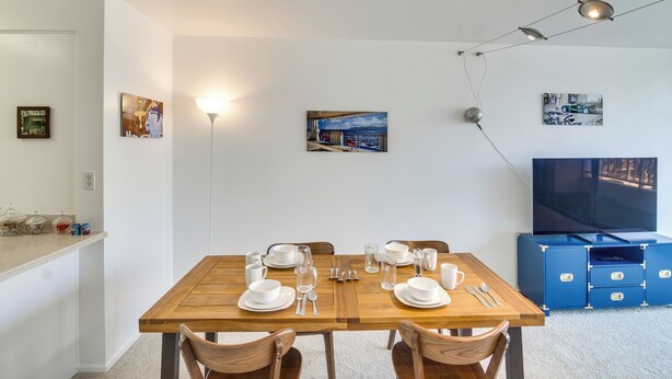 Ein Essbereich mit einem Holztisch, gedeckt für vier Personen, einem Fernseher an der Wand und einer Deckenleuchte.