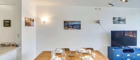 Et spiseområde med et træbord dækket til fire personer, et fjernsyn på væggen og en loftlampe.