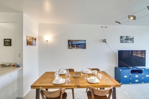 A dining area with a wooden table set for four, a TV on the wall, and a ceiling light fixture.