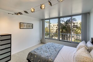 A bedroom with a large window, a bed with floral bedding, a dresser, and a framed picture on the wall. - Walk to Beach & Boardwalk! Condo in Santa Monica (Santa Monica)