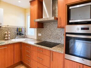 A kitchen with wooden cabinets, granite countertops, a built-in oven, and a microwave. - Winahost Piso Gavines (CASTELL-PLATJA D'ARO)