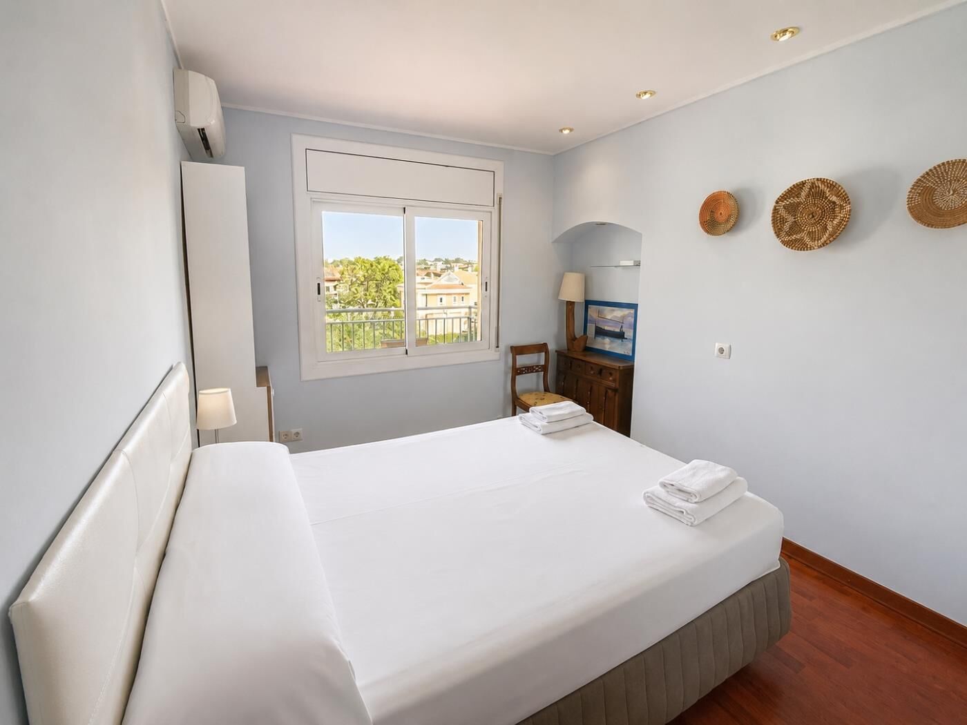 Um quarto com cama, janela, cadeira e luminária fixada na parede.