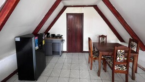 A small kitchen with a refrigerator, a coffee maker, and a cabinet. There is a wooden dining table with chairs and a door in the background. - Tranquil Cabin Getaway in San Ramón, Costa Rica (San Ramón)