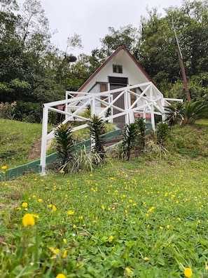 Un edifici blanc amb teulada vermella, envoltat de vegetació i flors grogues.