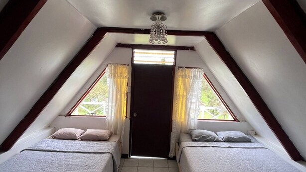 A small, triangular attic bedroom with two beds, a ceiling fan, and a door leading outside. - Tranquil Cabin Getaway in San Ramón, Costa Rica (San Ramón)