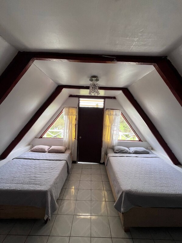 A small, triangular attic bedroom with two beds, a ceiling fan, and a door leading outside.