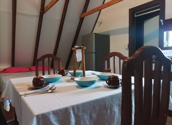 A dining table set with blue and brown bowls, spoons, and a teapot in a room with wooden beams and a window.