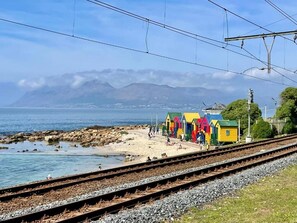 A coastal railway track with colorful beach huts and a mountainous backdrop.