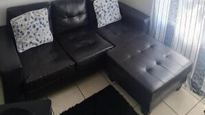 A living room with a black leather sofa, a black rug, and a window with curtains.