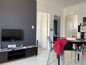 Una sala moderna con un televisor de pantalla plana, un mueble de entretenimiento oscuro y una zona de comedor con una mesa y sillas.