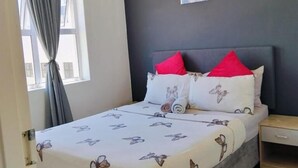 A bedroom with a bed, a nightstand, a window with curtains, and a wall-mounted picture.