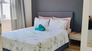 A bedroom with a bed, a nightstand, and a window with curtains.