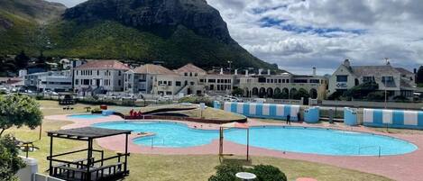 A swimming pool with a mountain backdrop, surrounded by buildings and a fenced area.