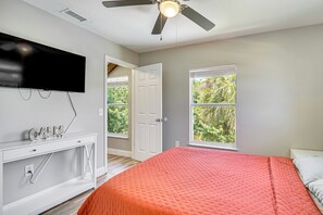 A bedroom with a bed, a television, a ceiling fan, and a window with a view of greenery. - 13 Mi to Beach! Family-Friendly Palm Bay Retreat (Palm Bay)