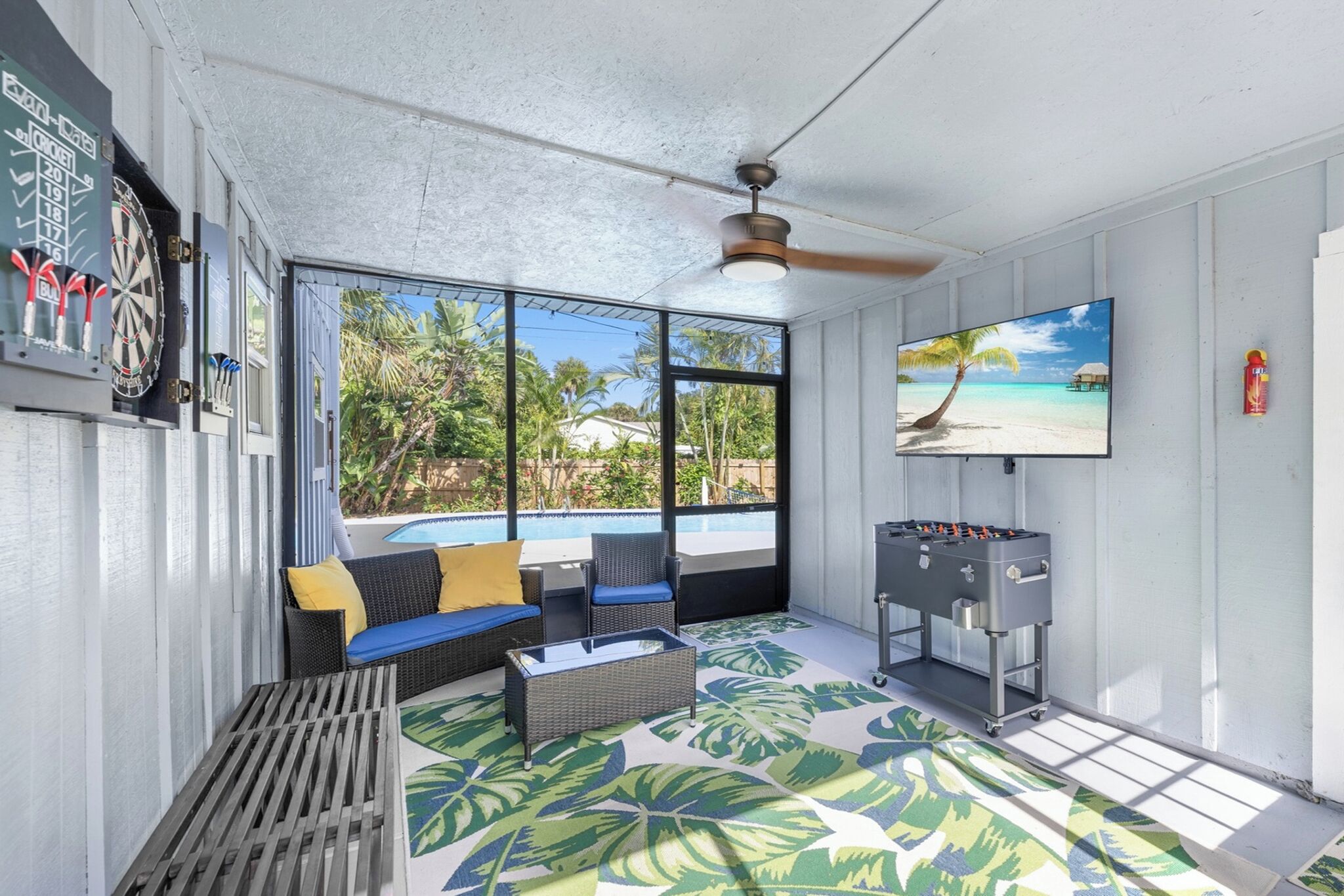 A room with a pool, a sofa, a television, and a dartboard.
