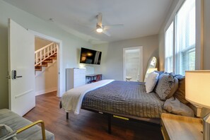 Un dormitorio con cama, escritorio, silla, televisor, ventilador de techo y una escalera.
