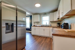 Una cocina moderna con armarios blancos, un refrigerador de acero inoxidable, encimeras de madera y un microondas integrado.