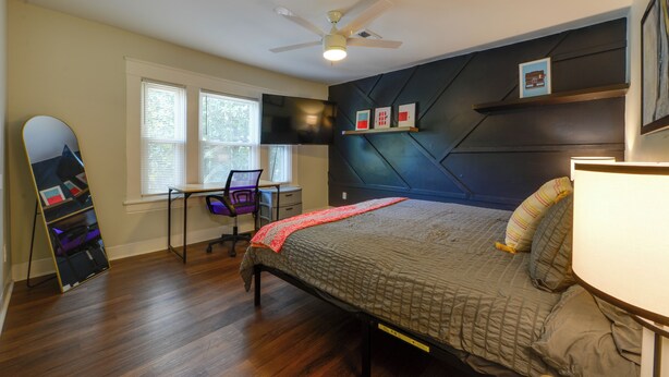 A bedroom with a bed, a desk with a chair, a ceiling fan, and a TV mounted on the wall. - 1 Mi to UNCG & Dtwn! Group Retreat w/ Private Yard (Greensboro)