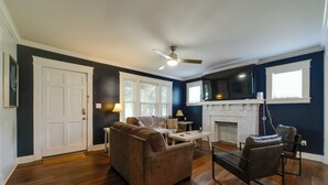 A living room with a fireplace, a ceiling fan, and a television mounted above it. - 1 Mi to UNCG & Dtwn! Group Retreat w/ Private Yard (Greensboro)